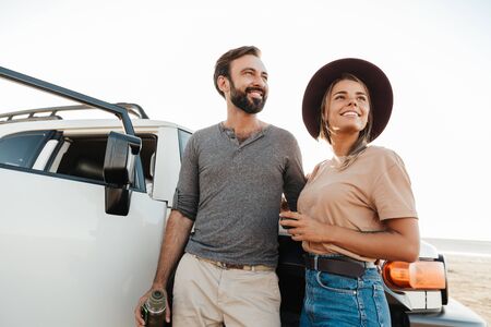 Photo of young positive happy loving couple outdoors at beach near car holding bottle with tea.の写真素材