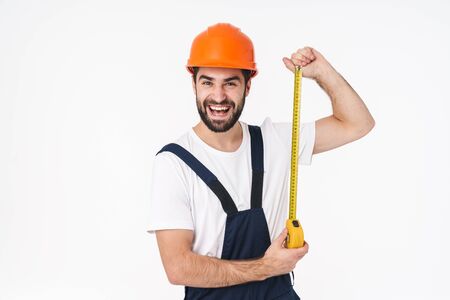 Photo of happy young man builder in helmet posing isolated over white wall background holding centimeter.の写真素材