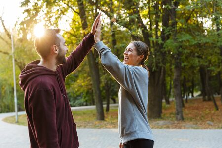 Photo of beautiful delighted couple in sportswear giving five while working out in green park during...