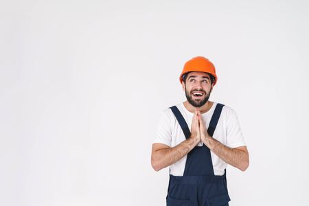 Photo of positive dreaming young man builder in helmet posing isolated over white wall background.の写真素材