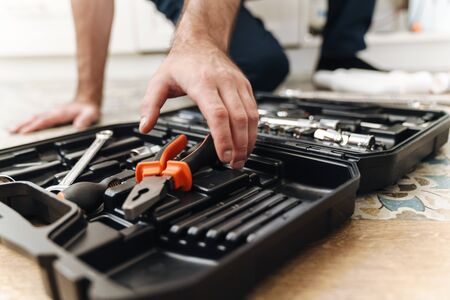 Cropped picture of young man plumber work in uniform indoors with case with equipment.の写真素材