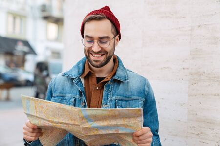 Close up of a handsome happy young stylish bearded man walking outdoors in the street, holding city...
