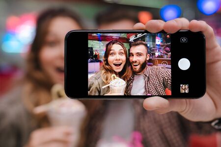 Image of a surprised optimistic amazing young loving couple sit in retro bright cafe take a selfie...