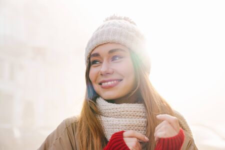 Close up of a cheerful pretty young girl wearing winter jacket and a hat standing on a city street