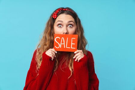 Image of surprised blonde woman holding placard and looking at camera isolated over blue background