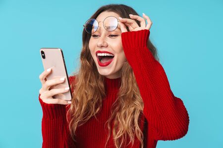 Image of joyful nice woman in eyeglasses using cellphone and smiling isolated over blue background