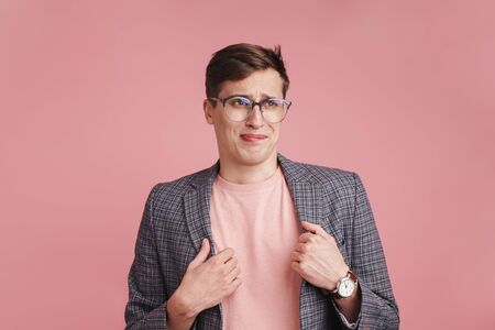 Photo of a young confused boy in glasses isolated over pink wall background.