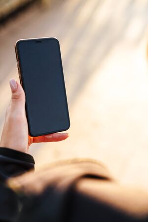 Cropped photo of young fitness woman using mobile phone outdoors.