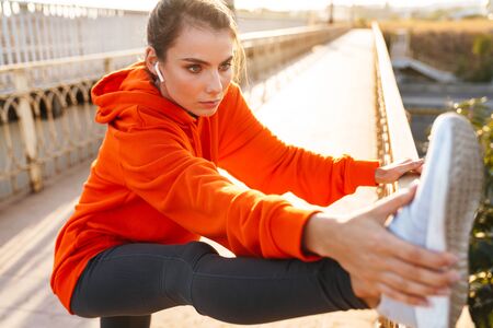 Picture of a pretty fitness woman outdoors listening music with earphones make stretsching...