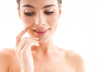 Beauty portrait of an attractive smiling young topless brunette woman standing isolated over white background, touching her faceの写真素材