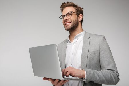 Portrait of smiling handsome man in eyeglasses holding and using laptop isolated over white backgroundの写真素材