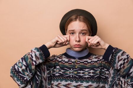 Photo of pretty unhappy woman in earrings crying and looking at camera isolated over beige backgroundの写真素材