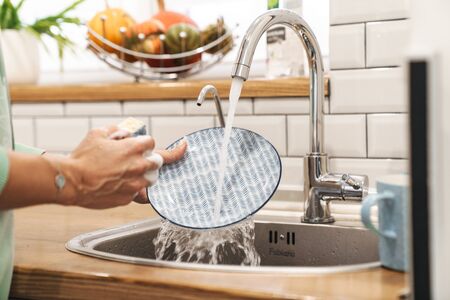 Cropped image of a young woman indoors at home wash the dishes at the kitchen.の写真素材