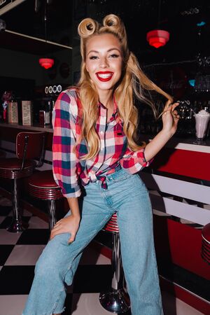 Photo of happy seductive woman with beautiful hairstyle laughing while sitting in retro american...