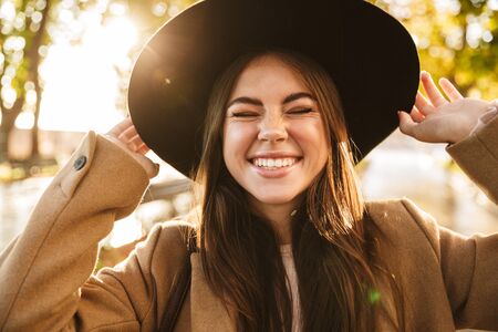 Portrait of caucasian young brunette woman wearing coat and hat walking in autumn parkの写真素材