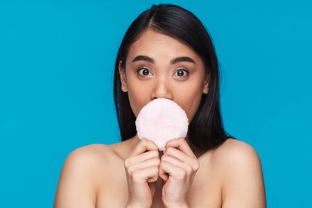 Photo of asian surprised young woman posing isolated over blue wall background holding powder puff.の写真素材