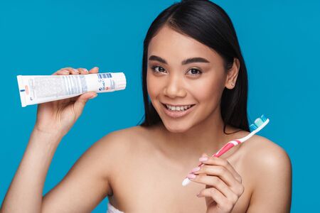 Photo of asian positive young woman posing isolated over blue wall background holding toothbrush and...