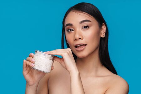 Photo of asian young woman posing isolated over blue wall background holding bath sea salt.の写真素材