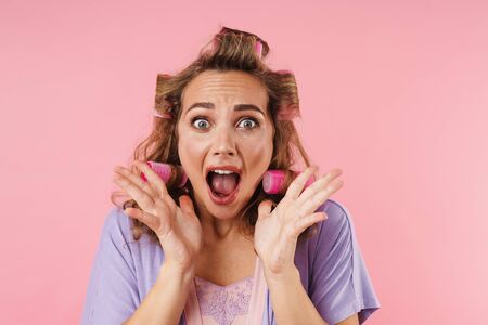 Image of young frightened woman in curlers screaming at camera isolated over pink backgroundの写真素材