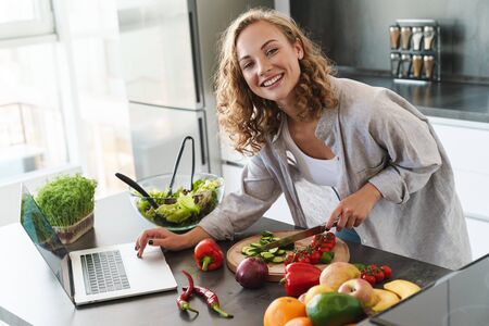 Happy young woman making a salad at the kitchen, chopping vegetablesの写真素材