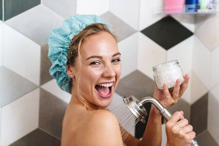 Image of young beautiful happy naked woman smiling while taking shower in bathroom at homeの写真素材