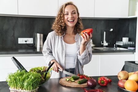 Happy young woman making a salad at the kitchen, chopping vegetables