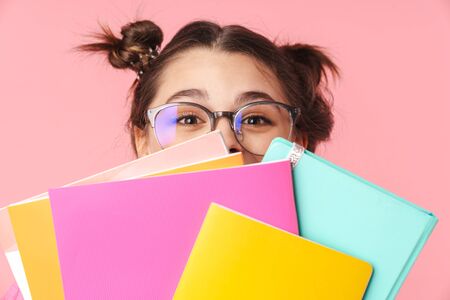 Photo amusing nice girl in eyeglasses covering her face with exercise books isolated over pink...