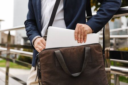 Close up of a man in formal wear taking his laptop out of the bag while standing outdoorsの写真素材