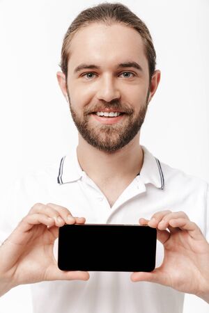 Photo of a young happy handsome bearded man posing isolated over white wall background using mobile...
