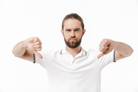 Attractive upset young bearded man wearing casual outfit standing isolated over white background,...
