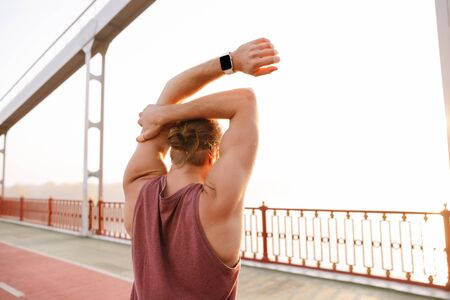 Attractive young fit sportsman working out on a bridge, doing stretching exercises