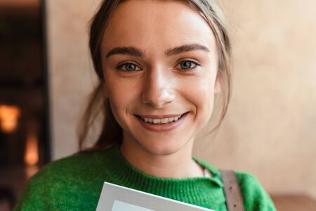 Photo of happy beautiful woman in green sweater looking and smiling at camera in cozy cafe
