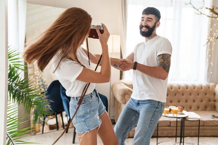 Image of romantic smiling couple taking retro photo while making fun in bright room at homeの写真素材