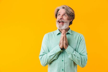 Picture of hopeful emotional elderly grey-haired bearded man in blue shirt posing isolated over...