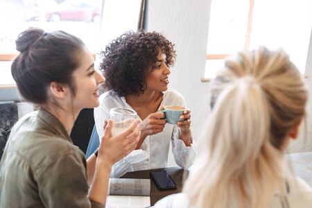 Group of multiethnic cheerful young women studying together at the coffee shopの写真素材