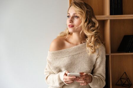 Image of a concentrated pretty beautiful young woman indoors at home using mobile phone.の写真素材