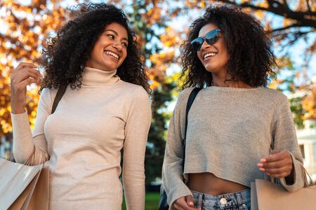 Two beautiful young stylish african women walking together at the street, talkingの写真素材