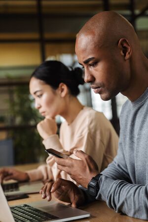 Image of multiethnic young female and male coworkers sitting at table and working on laptops in officeの写真素材