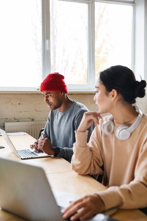 Image of a young concentrated multiracial colleagues indoors work in office with laptop computers.