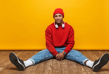 Portrait of an attractive confident casual young african man sitting on a floor over yellow...
