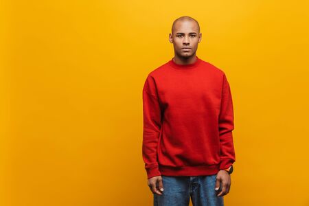Portrait of an attractive confident casual young african man standing over yellow background, looking at cameraの写真素材