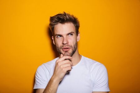 Attractive pensive young man wearing pullower standing isolated over yellow background, looking awayの写真素材