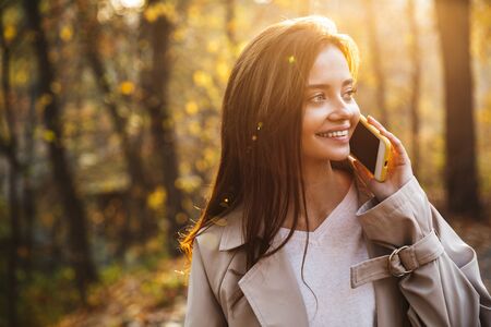 Image of young brunette woman in autumn coat smiling and walking in autumn park outdoorsの写真素材