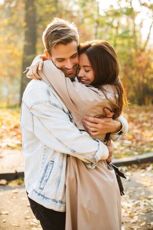 Image of attractive young caucasian couple smiling and walking through autumn park together