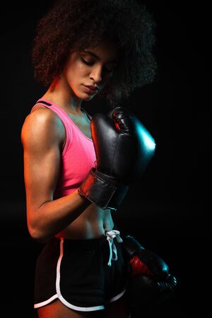 Image of young african american sportswoman working out in boxing gloves isolated over black backgroundの写真素材