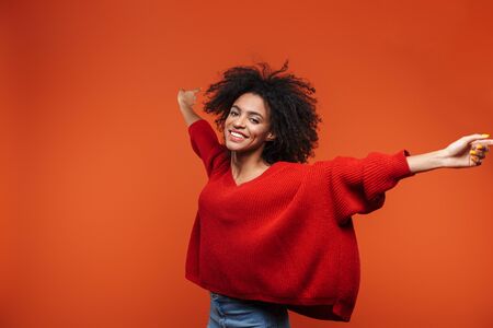 Beautiful cheerful young african woman wearing sweater standing islolated over red background, celebratingの写真素材