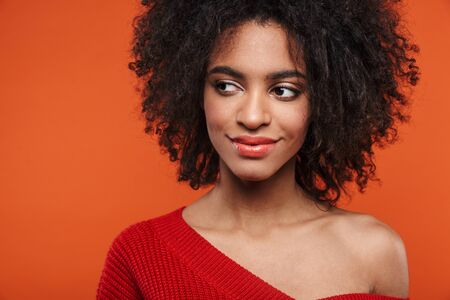 Beautiful smiling young african woman wearing sweater standing islolated over red background,...
