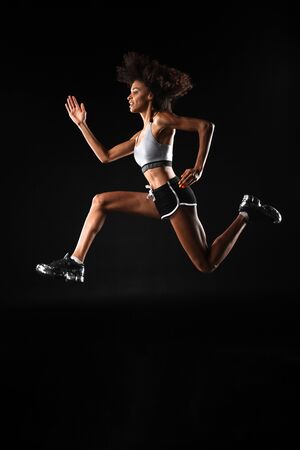 Image of smiling african american sportswoman doing exercise while working out isolated over black...
