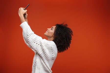 Smiling attractive young woman standing isolated over red background, taking a selfie