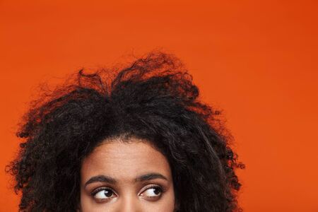 Close up half head portrait of a young african woman isolated over red background, looking awayの写真素材